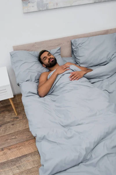 Vista ad alto angolo di giovane uomo afroamericano con gli occhi chiusi dormire a letto — Foto stock