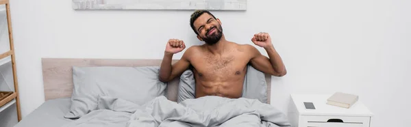 Homem americano africano sem camisa com cabelo tingido esticando na cama, bandeira — Fotografia de Stock