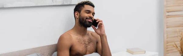 Hemdloser afrikanisch-amerikanischer Mann mit gefärbten Haaren, der im Schlafzimmer auf dem Handy spricht, Banner — Stockfoto