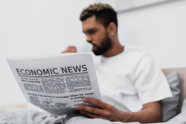 Homme afro-américain flou avec les cheveux teints boire du café tout en tenant journal au lit — Photo de stock