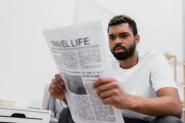 Serious african american man with dyed hair reading blurred travel life newspaper — Stock Photo