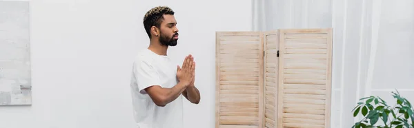 Bärtiger afrikanisch-amerikanischer Mann meditiert mit betenden Händen in der Nähe von Klappbildschirm, Banner — Stockfoto
