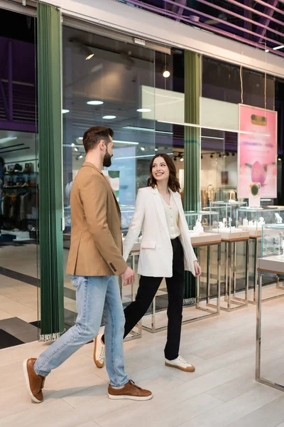 Улыбающаяся пара, идущая рядом с витринами ювелирного магазина — стоковое фото