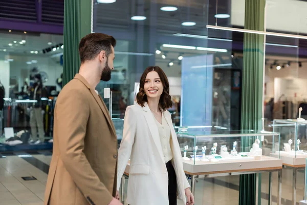 Mujer sonriente mirando al novio mientras camina en la joyería - foto de stock