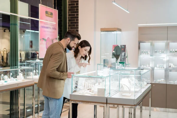 Jeune femme pointant du doigt les bijoux près du petit ami dans le magasin — Photo de stock