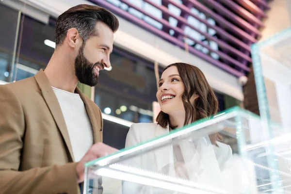 Low angle view o smiling couple looking at each other near showcase in jewelry shop — Stock Photo