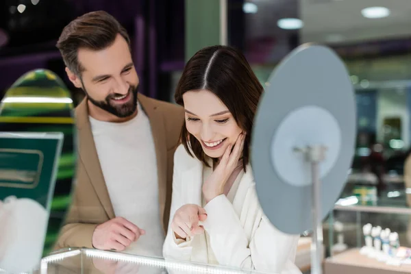 Lächelnde Frau zeigt auf Schaufenster neben verschwommenem Freund in Schmuckgeschäft — Stockfoto