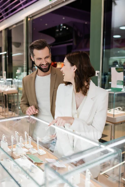 Femme joyeuse pointant du doigt la vitrine et regardant petit ami dans la bijouterie — Photo de stock