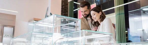 Mujer joven eligiendo accesorios cerca de novio en la joyería, bandera - foto de stock