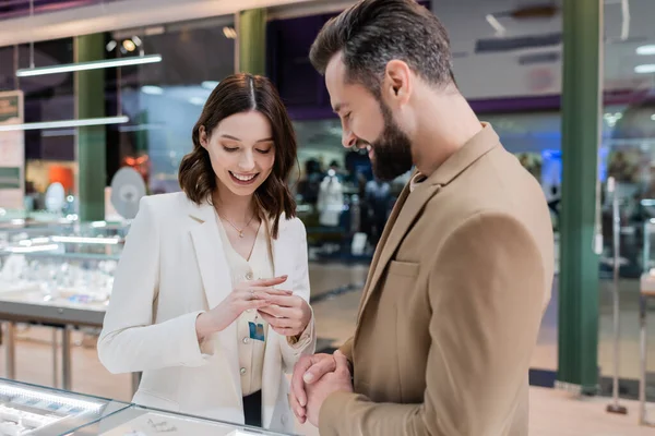 Mujer alegre usando anillo cerca de novio en joyería - foto de stock