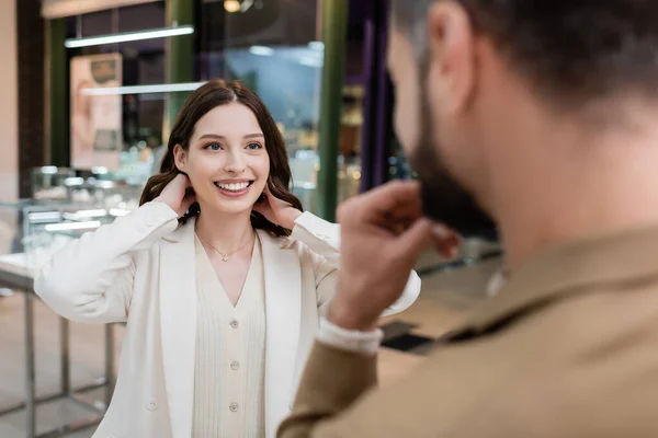 Donna positiva che indossa collana vicino fidanzato offuscata in gioielleria — Foto stock