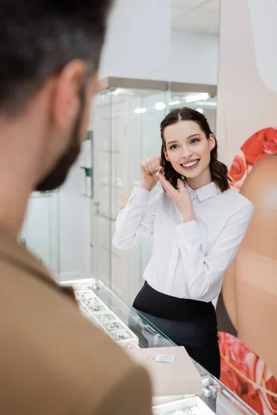 Lächelnder Verkäufer hält Schmuck neben verschwommenem Mann im Geschäft — Stockfoto