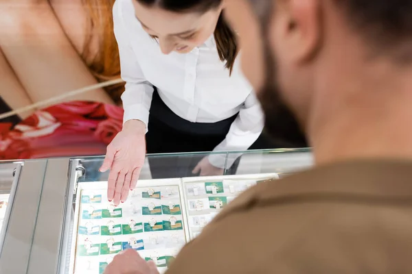 Seller pointing at jewelry rings in showcase near blurred customer in shop — Stock Photo