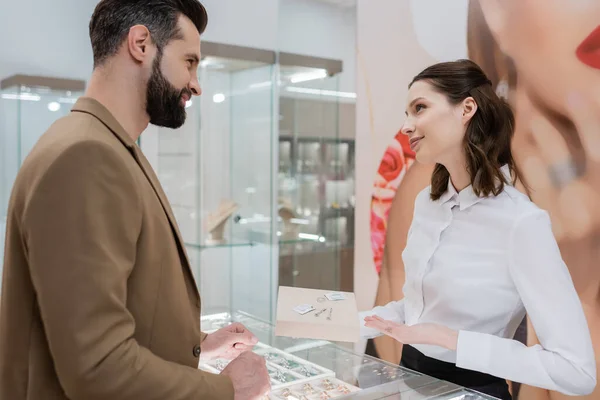 Side view of customer looking at seller pointing with hand at jewelry in shop — Stock Photo