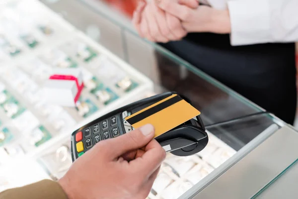 Vista recortada del hombre que paga con tarjeta de crédito cerca del vendedor borroso en la joyería - foto de stock