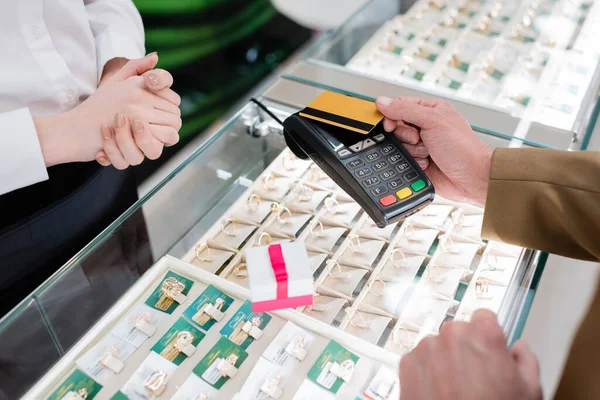 Vista ritagliata del cliente che paga con carta di credito vicino regalo e venditore in gioielleria — Foto stock