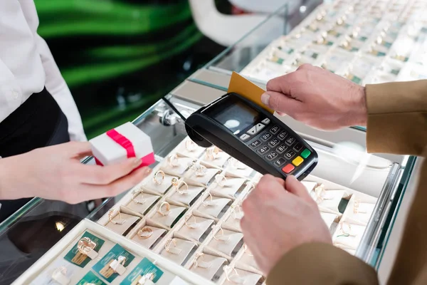 Ausgeschnittene Ansicht eines Mannes, der mit Kreditkarte zahlt, in der Nähe eines Verkäufers, der eine Geschenkschachtel in einem Juweliergeschäft hält — Stockfoto