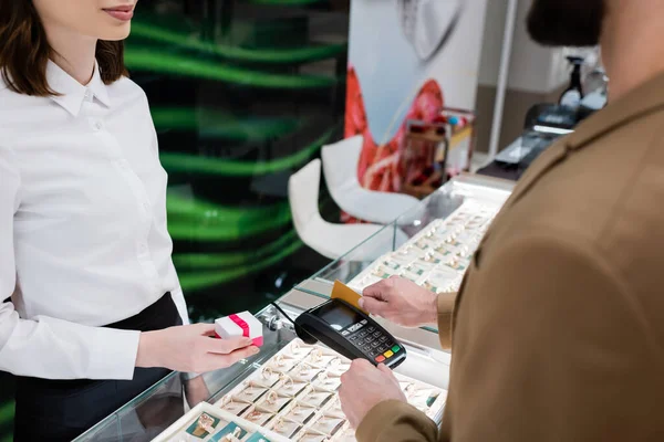 Cropped view of seller holding gift near customer paying with credit card in jewelry shop — Stock Photo