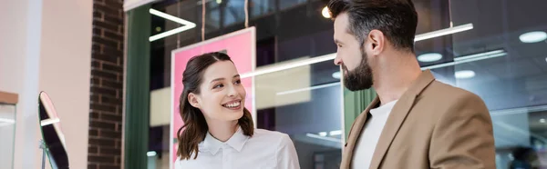 Fröhlicher Verkäufer schaut Kunden in der Nähe von Spiegel im Juweliergeschäft an, Banner — Stockfoto