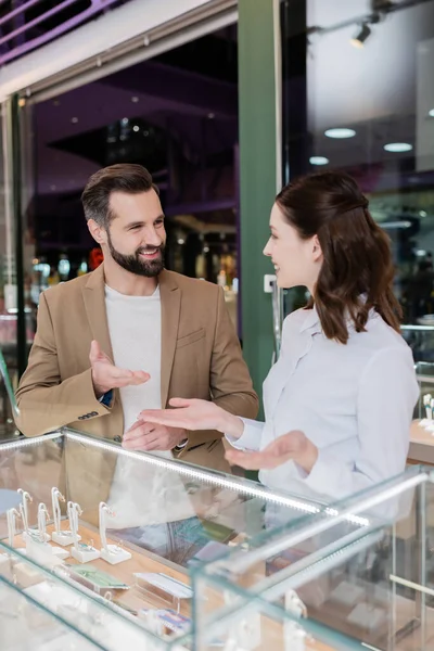 Cheerful customer and seller pointing with hands near jewelry in showcase in shop — Stock Photo