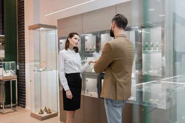 Bearded customer standing near showcase and seller in jewelry shop — Stock Photo