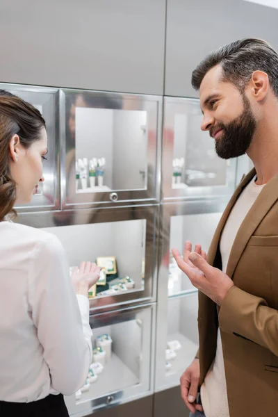 Smiling customer pointing at blurred showcase near seller in jewelry shop — Photo de stock