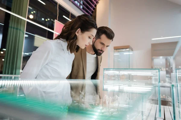 Bärtiger Kunde wählt Schmuck in der Nähe des Verkäufers im Geschäft — Stockfoto