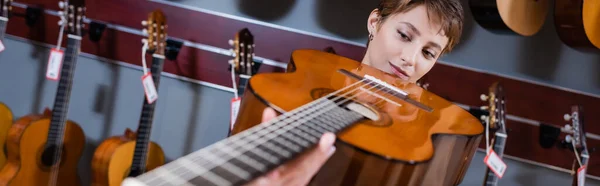 Musician looking at blurred acoustic guitar in music store, banner — Foto stock