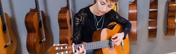 Young woman playing acoustic guitar in music shop, banner — Photo de stock