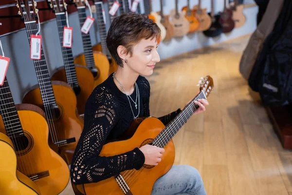 Side view of young smiling musician playing acoustic guitar in music shop — Stockfoto