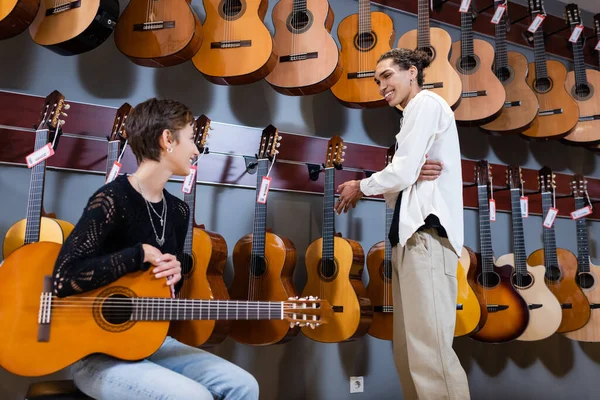 Smiling woman holding acoustic guitar near african american seller in instrumental music store — Stock Photo