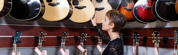 Вид сбоку клиента, смотрящего на акустическую гитару в музыкальном магазине, баннер — стоковое фото