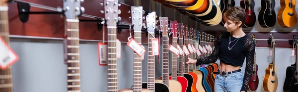 Jeune femme choisissant la guitare acoustique dans le magasin musical, bannière — Photo de stock