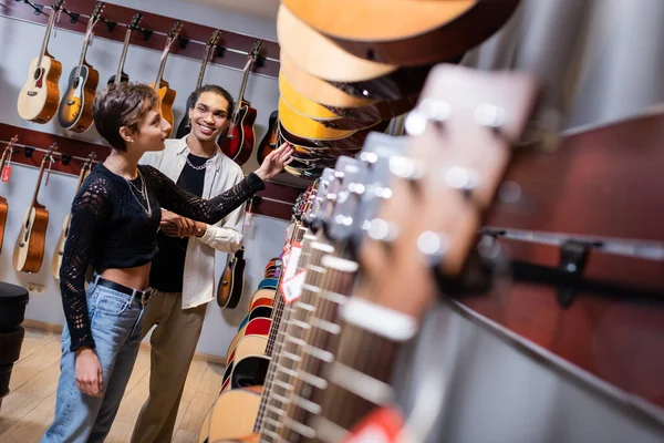 Молодая женщина выбирает акустическую гитару рядом с африканским продавцом в музыкальном магазине — стоковое фото