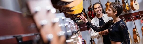 African american seller looking at woman choosing acoustic guitar in music store, banner — Stock Photo