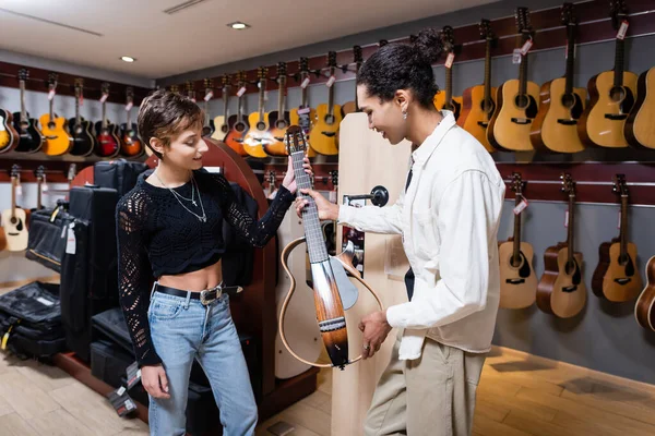 KYIV, UKRAINE - FEBRUARY 16, 2022: African american seller holding electric guitar near smiling customer in music shop — Stock Photo