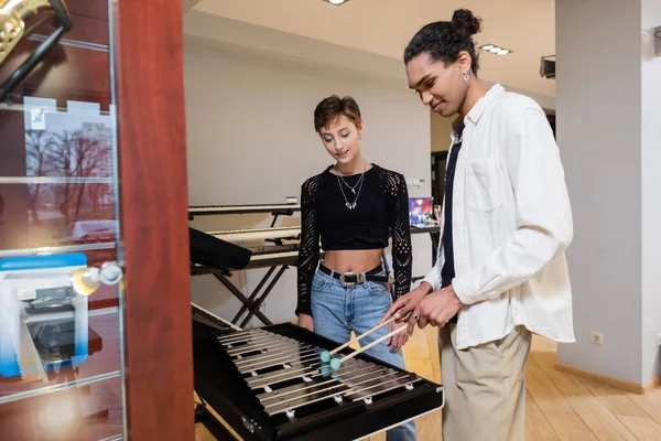 Vendedor afroamericano jugando xilófono cerca del cliente en la tienda de música - foto de stock