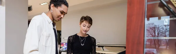 Smiling interracial seller and customer standing in music store, banner — Stock Photo