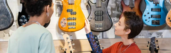 KYIV, UKRAINE - FEBRUARY 16, 2022: African american buyer and seller looking at electric guitars in store, banner — Stock Photo