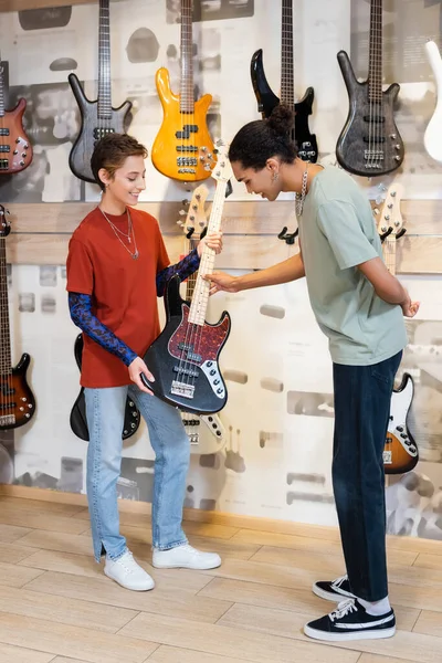 KYIV, UKRAINE - 16 FÉVRIER 2022 : Un client afro-américain souriant touche une guitare électrique près d'un vendeur dans un magasin de musique — Photo de stock