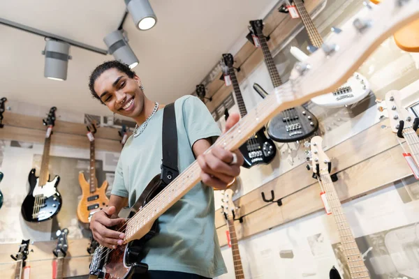 KYIV, UKRAINE - 16 FÉVRIER 2022 : Vue en angle bas de joyeux acheteur afro-américain jouant de la guitare électrique dans le magasin de musique — Photo de stock