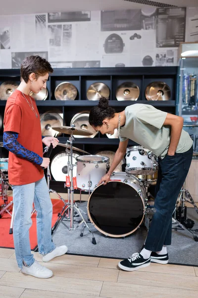 Side view of african american customer touching drum set near seller with drumsticks in music store — Stock Photo