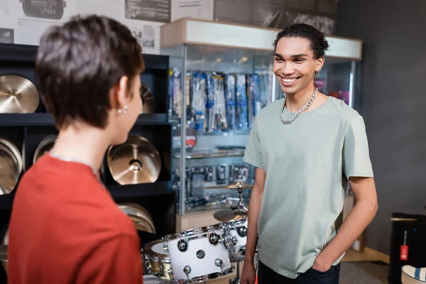 Sorridente cliente afroamericano guardando venditore offuscata in negozio di musica — Foto stock