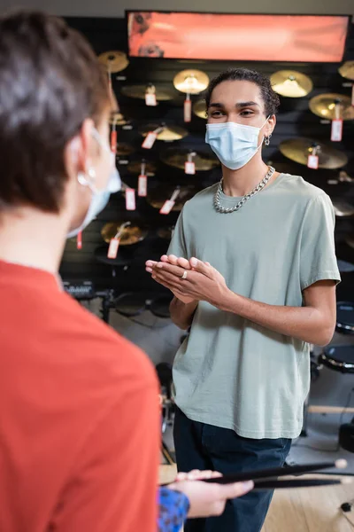 African american customer in medical mask standing near blurred seller with drumsticks in store — Photo de stock