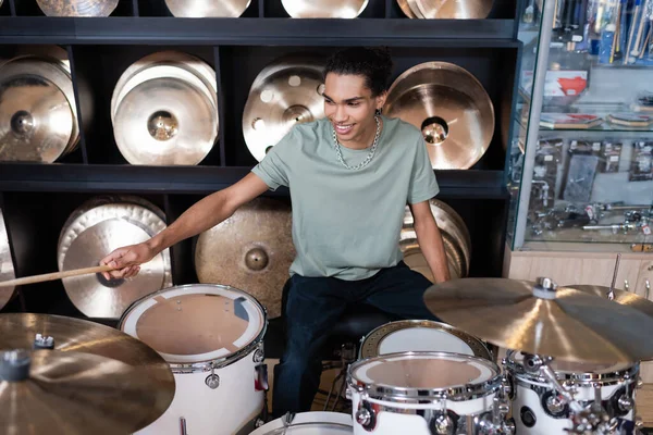 Un client afro-américain souriant joue de la batterie dans un magasin de musique — Photo de stock