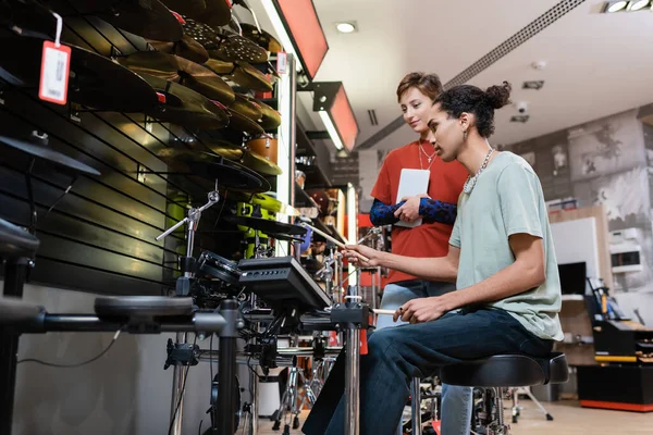 Afroamerikaner spielt in Musikladen mit digitalem Tablet in der Nähe eines Verkäufers elektronisches Schlagzeug — Stockfoto