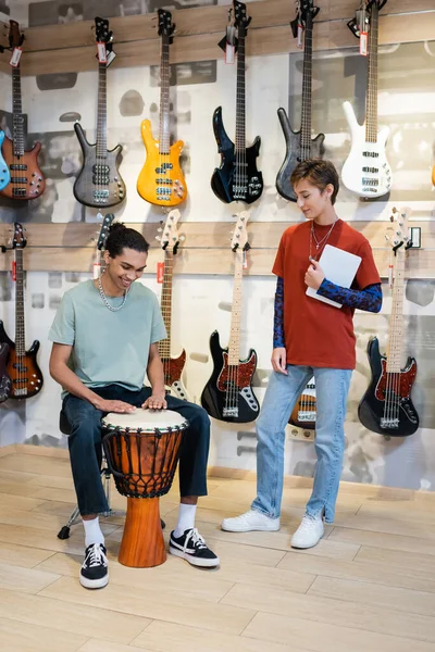 KYIV, UKRAINE - 16 FÉVRIER 2022 : Un client afro-américain joue au djembé près du vendeur avec une tablette numérique dans un magasin de musique — Photo de stock