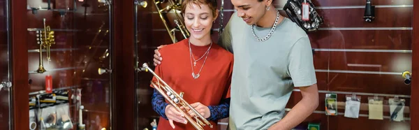 Junger afrikanisch-amerikanischer Mann umarmt Freundin und blickt auf Trompete im Musikladen, Banner — Stockfoto