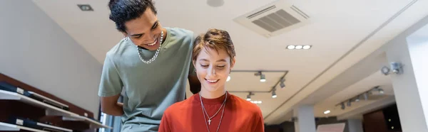 Smiling african american man looking at girlfriend in music store, banner — Stockfoto