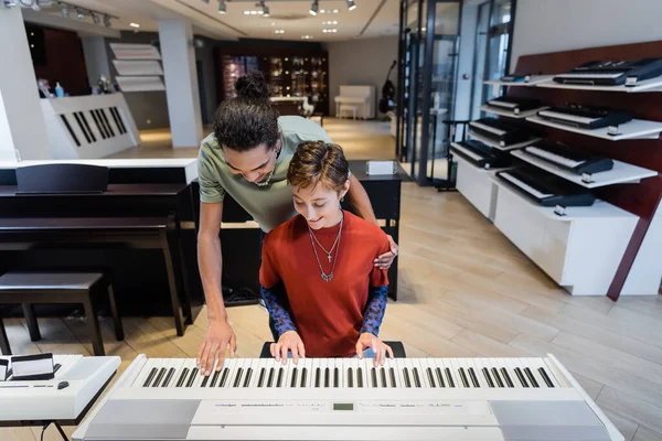 Smiling multiethnic couple playing synthesizer together in music store — Stock Photo